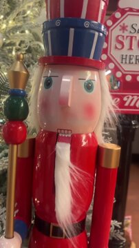 vertical video of wooden nutcracker with stacked hat beside frosted christmas tree in festive scene
