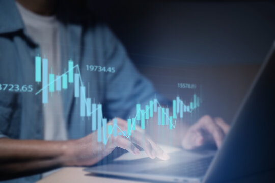 A man is using a laptop or smartphone to stock trading graph, graphic overlay laptop keyboard, finance and investment concept. Economy trends for business, financial charts and digits. - Powered by Adobe