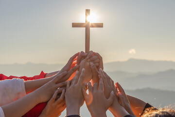 Silhouette family hands praying and holding Christian cross for worshipping God on mountain at sunrise background. Christian, Christianity, Religion copy space background. Easter Sunday concept: