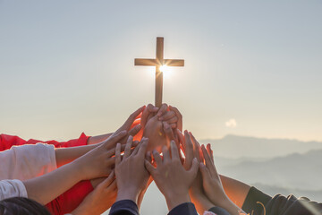 Silhouette family hands praying and holding Christian cross for worshipping God on mountain at sunrise background. Christian, Christianity, Religion copy space background. Easter Sunday concept: