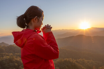Cute girl holding hands praying to god on mountain sunset background