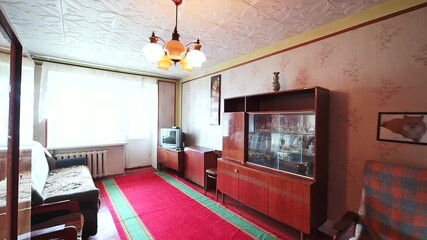 living room features a vintage design with floral wallpaper, a patterned ceiling, a wooden cabinet with glass doors, a red carpet, a sofa, and a chandelier. The room exudes a warm and nostalgic atmosp