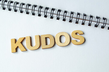 Top view of KUDOS wooden letters on white notepad.