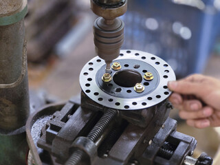 Focused close up of mechanic hand at workshop using drill press machine. skilled worker performs precision metalworking, drilling hole in steel brake disc for repair