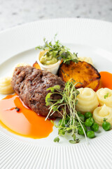 Elegant plated meal with meatloaf, creamy potatoes, green peas, roasted sweet potato, and delicate garnishes on a white plate in a modern setting