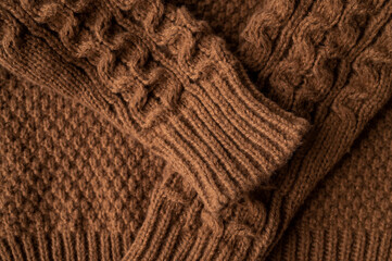 Close-up of brown knitted wool cotton sweater. Details of cozy winter or fall children's sweater, buttoned cardigan, pullover. Neckline detail, sleeves, large knit pattern. Trendy Color 2025