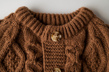 Close-up of brown knitted wool cotton sweater. Details of cozy winter or fall children's sweater, buttoned cardigan, pullover. Neckline detail, sleeves, large knit pattern. Trendy Color 2025