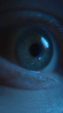Macro view of a nervous human eye looking at display, illuminated by blue smartphone screen light, representing anxiety, social media addiction, and late-night doom scrolling. Vertical video