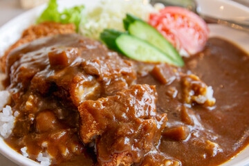 Close-up of popular Japanese Katsu Curry, featuring crispy fried pork cutlet and rich, thick curry sauce over white rice. Served with fresh side vegetables. Traditional Asian comfort food.