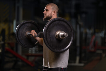 man is lifting a barbell while doing a bicep curl in a gym setting. The workout takes place in the morning. He focuses on strength training to improve fitness.