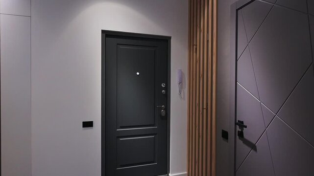 Modern entryway with a sleek black front door and a grey interior door, separated by a wooden slat accent wall. Recessed lighting creates a stylish, minimalist ambiance