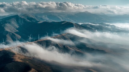 Obraz premium Majestic Aerial View of Wind Turbines on Rolling Mountains Surrounded by Mysterious Fog and Dramatic Clouds Under a Clear Blue Sky