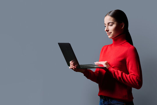 Portrait of smiling teenage girl using laptop on gray studio background - Powered by Adobe