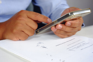 A businessman scrolls through his phone at his desk, uses social media, browses, and surfs the internet. Business concepts and technological advancements
