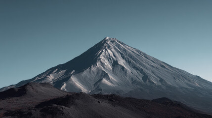 An impressive mountain peak, partially covered with snow, rises dramatically against a clear blue sky, showcasing its rugged beauty and serene atmosphere.