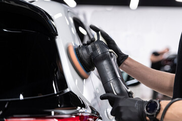Close-up of ceramic coating being applied by hand to a black car rear body panel, highlighting precise technique, paint protection, deep gloss and professional car detailing process.