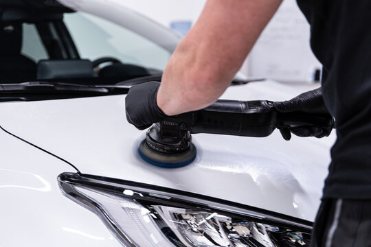 Close-up of machine polishing and paint correction on a white car hood near the headlight, showing surface refinement, gloss enhancement and preparation for coating in a detailing studio.
