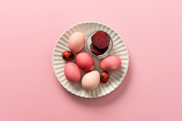 A variety of dyed Easter eggs in soft pink and vibrant shades rest on a decorative plate, a small bowl of beets, a way to dye eggs pink, ready for an Easter celebration filled with joy