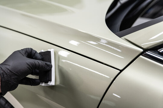 Close-up of ceramic coating being applied by hand to a car body panel with an applicator pad, showing precision work, paint protection and professional car detailing process.