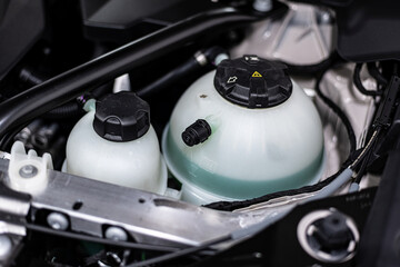 Close-up of a coolant expansion tank inside a car engine bay, showing automotive cooling system components during routine vehicle inspection, maintenance and technical service.
