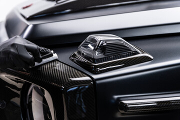 Close-up of ceramic coating being applied to a carbon fiber exterior element on a luxury car, highlighting precision work, surface protection, deep gloss and premium car detailing service.