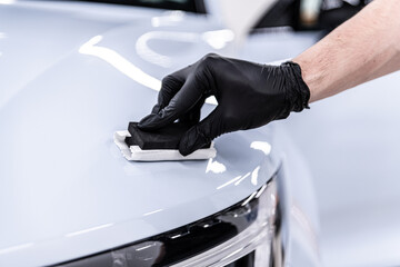 Close-up of ceramic coating being applied by a gloved detailer to a white car hood and front body panel, showing precision work, paint protection and premium car detailing service.