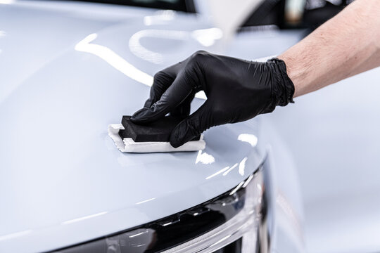 Close-up of ceramic coating being applied by a gloved detailer to a white car hood and front body panel, showing precision work, paint protection and premium car detailing service.