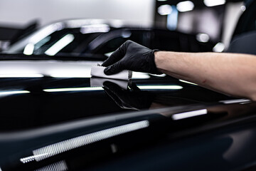 Close-up of ceramic coating being applied to a glossy black car by a gloved detailer inside a...