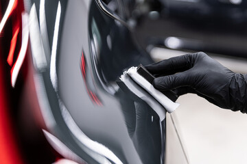 Close-up of ceramic coating applied with an applicator pad on a car body panel, showing precision work, high gloss finish, paint protection and professional car detailing process.