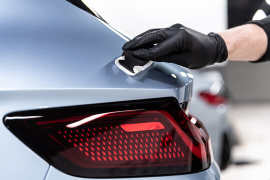 Close-up of ceramic coating being applied to a blue car body panel near the rear taillight by a gloved detailer, highlighting precision work, paint protection and premium detailing service.