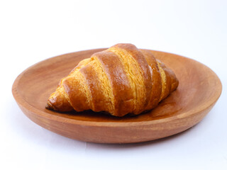 Buttery golden croissant placed on a wooden plate isolated on white background