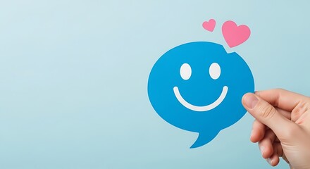 Hand holding a blue speech bubble with a happy smiley face and pink hearts against a light background
