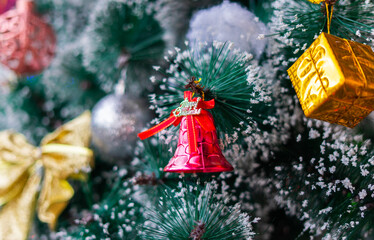 Festive Christmas ornaments hanging on a snowy pine tree. Glittery red and silver baubles, a gold bow, and a bell decorate the frosted green branches.