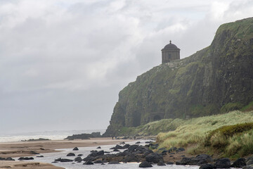 Panoramic low angle view during storm over Downhill Beach in Coleraine, Nothern Island with people walking in background and 1785 built Mussenden Temple high on cliff