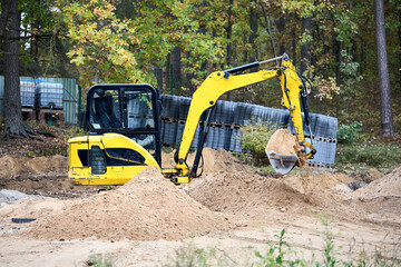 Mini excavator at construction site surrounded by trees. Compact construction equipment for operative earthworks. Tracked yellow and black mini excavator digger.