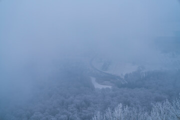 Germany, Foggy aerial panorama view above fields curved street tree tops and white snow covered nature landscape above the forest winter wonderland