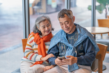 asian senior couple using smartphone surfing internet online together in coffee shop,concept of elderly people with modern lifestyle