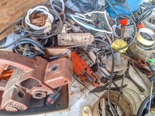 A jumbled mess of old, broken tools, tangled electrical cords, and workshop debris, including a disassembled power tool housing and  electric motor.
