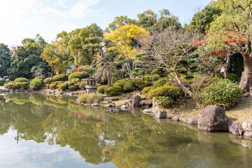 Visitors walk along the scenic path by the pond in a Japanese garden during a sunny afternoon in autumn