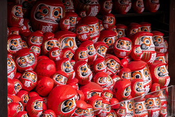 Many daruma dolls displayed in a shop on a sunny day in Japan during a busy market scene