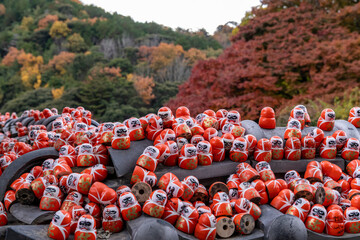 Colorful daruma dolls on a stone altar in a forested area during autumn
