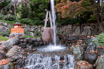 Water flows over rocks in a garden with small lights and trees at a shrine during autumn