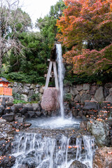 Waterfall flows down rocks surrounded by trees in a garden area with autumn leaves present