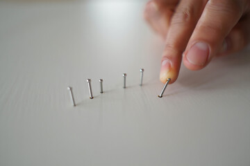 Finger Touching One of Small Silver Pins in Row on White Surface at Eye Level 150 characters