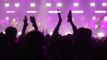 Silhouetted people enjoying a live concert with hands raised and clapping under energetic purple stage lights