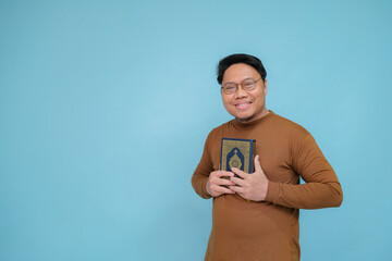 Fototapeta premium Portrait of an Asian Muslim man embracing the holy book of the Koran wearing brown shirt and glasses, the holy book of the Koran is guide for life.