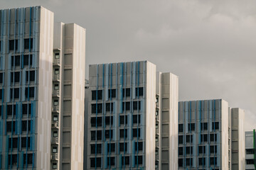 A row of modern apartment buildings with blue accents under a cloudy sky. The buildings are tall and feature a grid-like facade.