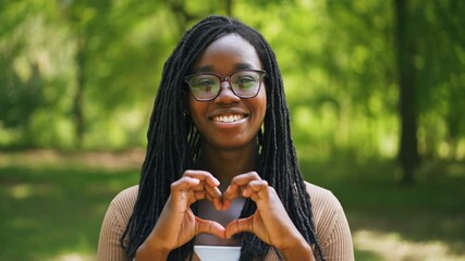 A woman making a heart shape with her hands, radiating love and positivity. Her genuine smile reflects warmth and affection.  Stock video