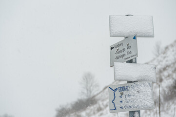 Wegweiser in Schneelandschaft aufsteigender Wanderweg Gustav-Str&ouml;hmfeld-Weg und Eduard M&ouml;rike Weg am ehemaligen Vulkanschlot Jusiberg in Kohlberg mit kahlen B&auml;umen vor grauem Himmel.