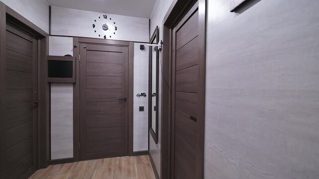 Modern hallway with light wood flooring, white textured walls, and dark brown doors. Recessed ceiling lights illuminate the space, featuring a wall clock and motivational poster